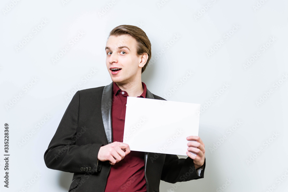 Smiling young european business man in red polo shirt and blazer holding blank A4 signboard. Business background with copy space mockup Smiling young european business man in red polo shirt and blazer holding blank A4 signboard. Business background with copy space mockup