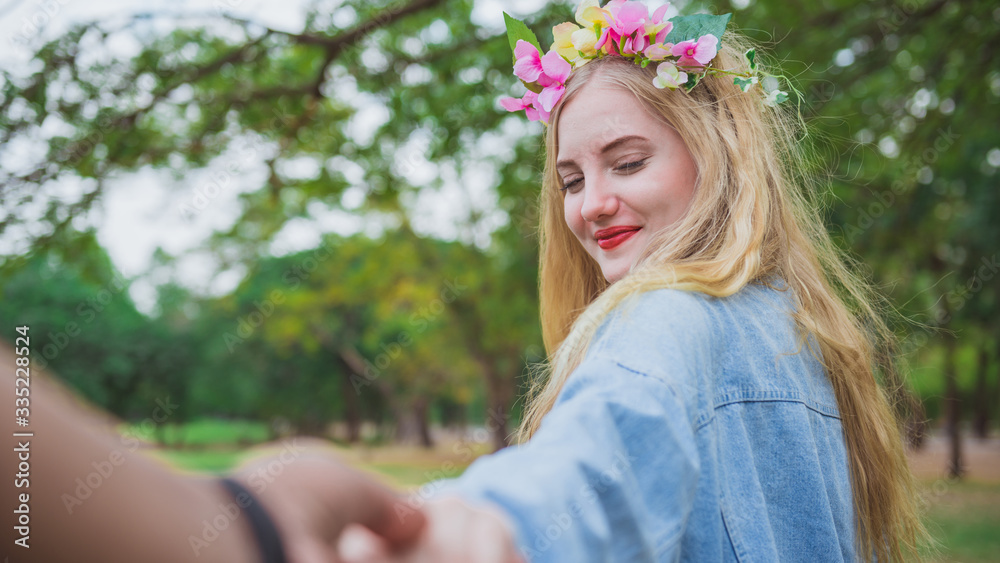 Fototapeta premium Young woman holding man hand leading in public park in vacation