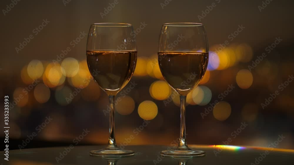 Charming still life shot of two glasses with wine against blurred background with warm yellow lights in bokeh Charming still life shot of two glasses with wine against blurred background with warm yellow lights in bokeh
