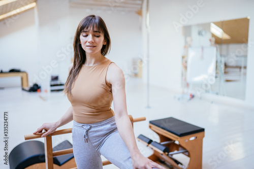 Portrait of female owner of small pilates studio wearing sportwear posing on sports equipment.