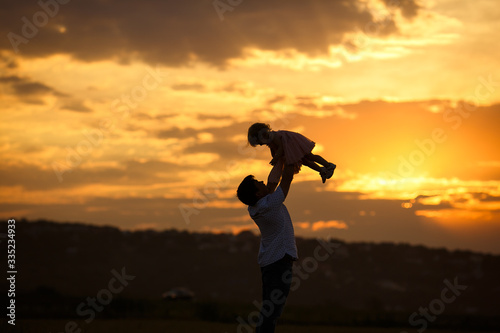 father throws up daughter in field at sunset. the 