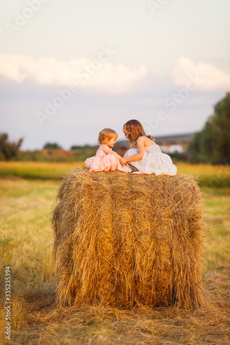 small girls sit on haystack wheat field sunset