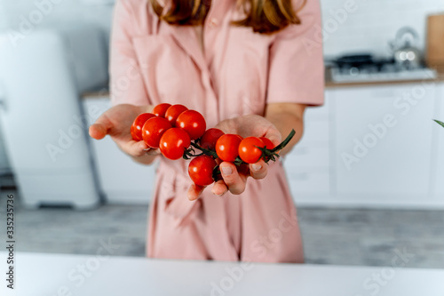 Housewife holding ripe cherry tomatoes in hands. Kitchen background. Pink dress on woman. Homefood concept. photo