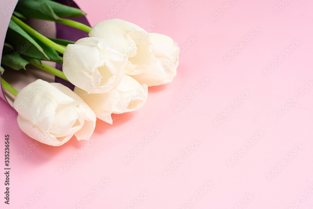 Fototapeta premium Bouquet of white tulips wrappen in pink paper. Minimal nature flat lay. Greeting card for Mother's Day and March 8th. Tender concept of spring holidays