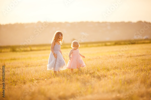 little girls going on sloping wheat field sunset