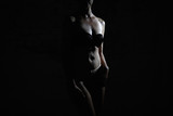 Half-naked sexy woman in lingerie, black top, light bottom in a dark room. Beautiful gentle shadows on the girl's body.