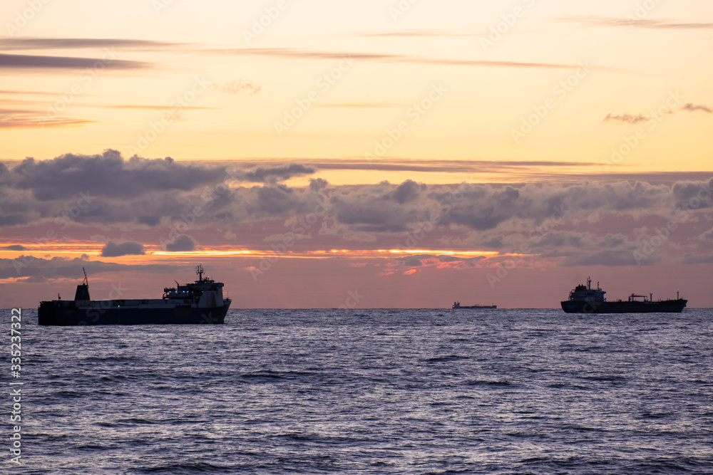 Orange sunset over the sea. Industrial ship on the roadstead. Beautiful clouds in the sky. Cargo transportation by sea. Marine