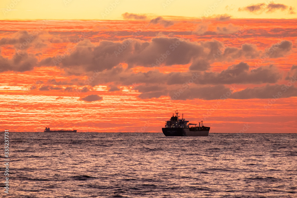Orange sunset over the sea. Industrial ship on the roadstead. Beautiful clouds in the sky. Cargo transportation by sea. Marine Orange sunset over the sea. Industrial ship on the roadstead. Beautiful clouds in the sky. Cargo transportation by sea. Marine