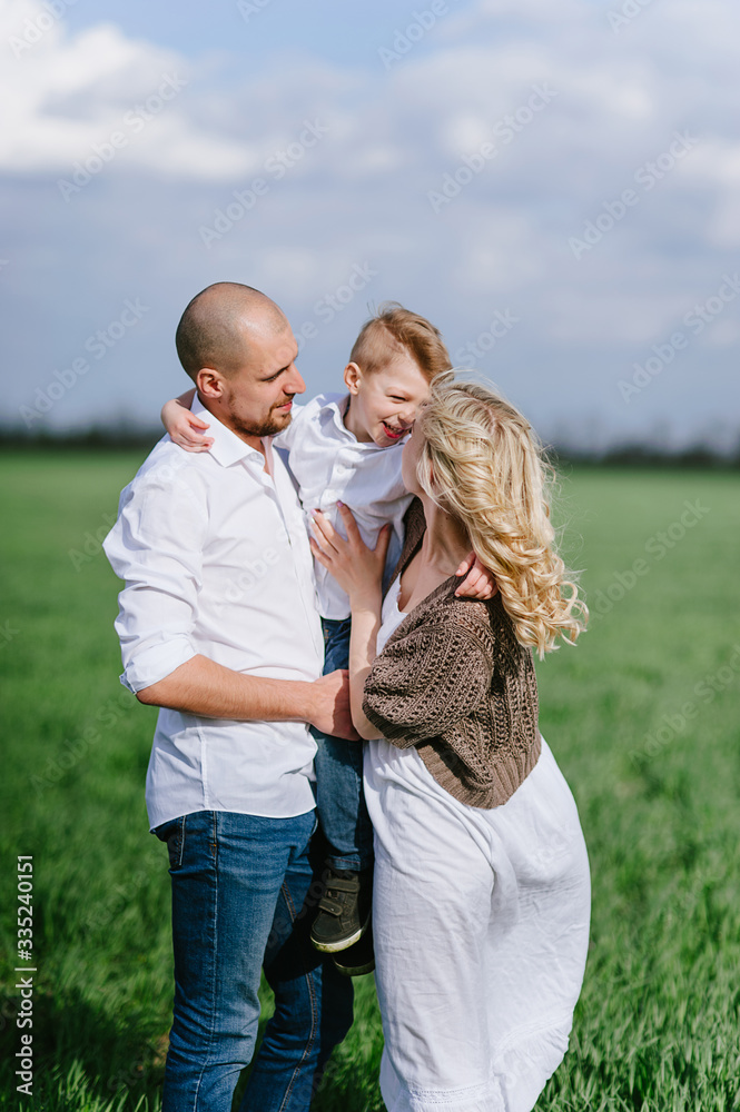 Family on a walk in a field with green grass and blue sky, early spring, good weather, happy family, white clothes Family on a walk in a field with green grass and blue sky, early spring, good weather, happy family, white clothes