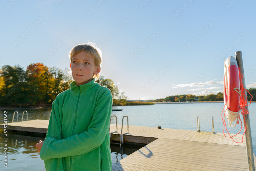 Young handsome boy thinking at wooden pier near the river
