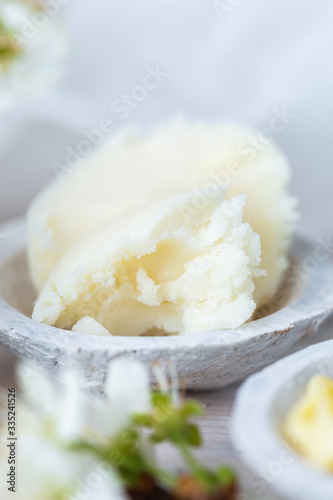 Shea butter on a white coconut cup on a white table in spring time. Karite cream for skin care. Raw home made butter for skin care.