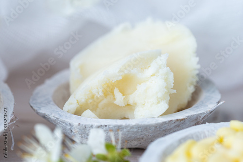 Shea butter on a white coconut cup on a white table in spring time. Karite cream for skin care. Raw home made butter for skin care.