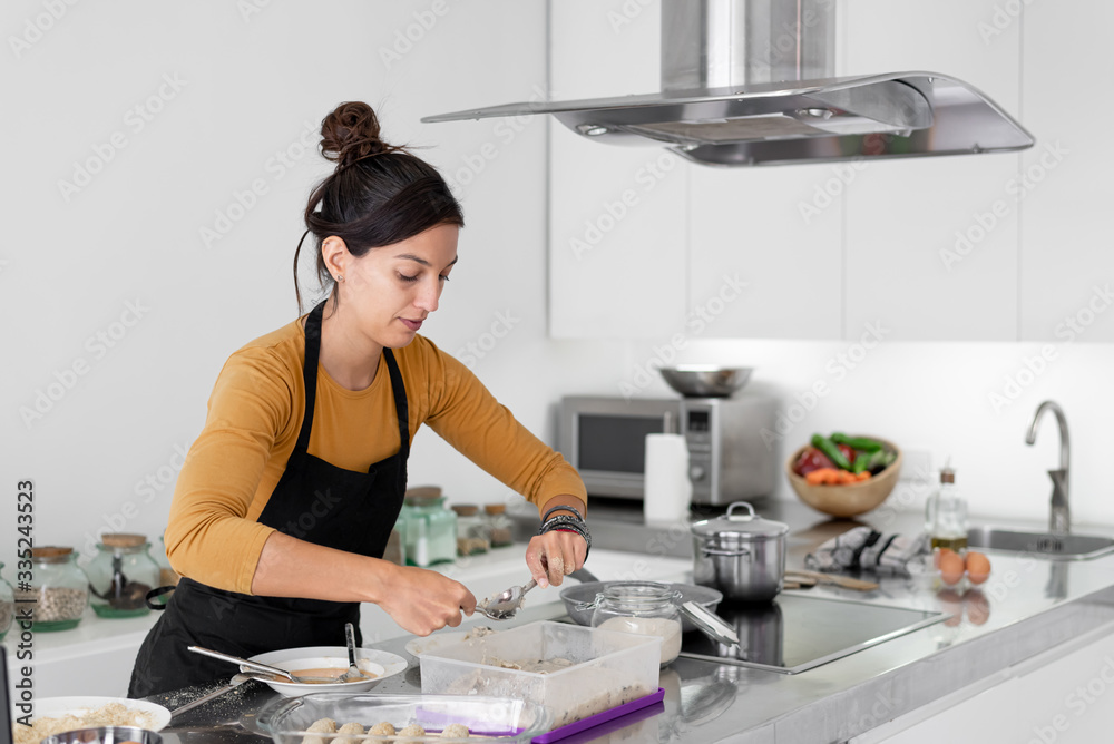 Young brunette woman with an apron cooking homemade croquettes in a modern kitchen Young brunette woman with an apron cooking homemade croquettes in a modern kitchen
