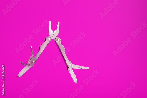 Multitool is a multi-functional tool on a pink background. The concept of an open, flying multi-tool with free space.