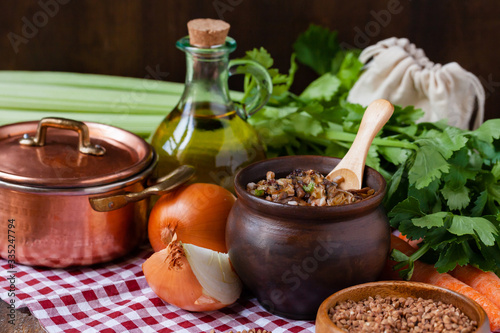 Traditional russian simple vegan meal: cooked buckwheat porridge with fried mushrooms and vegetables in clay pot. Healthy food, low calories, easy to cook. Copper pan, wooden backround, close up 