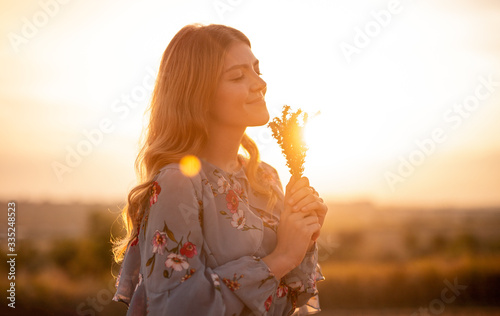 Happy woman with flowers enjoying sunset in field