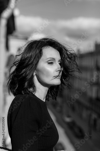 Stylish woman in black stands on the city balcony