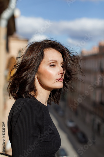 Stylish woman in black stands on the city balcony