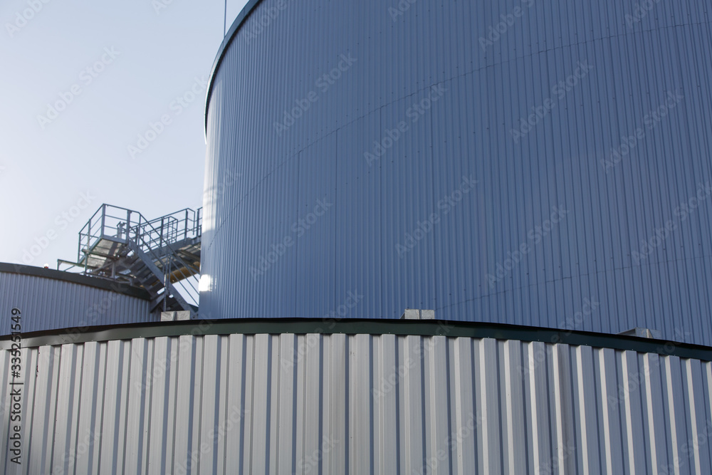 Obraz premium part of the metal industrial tanks outdoor. roof of technological building at the industrial plant on background. Equipment and appliances at the gas company. metal ladder stairs on the tank
