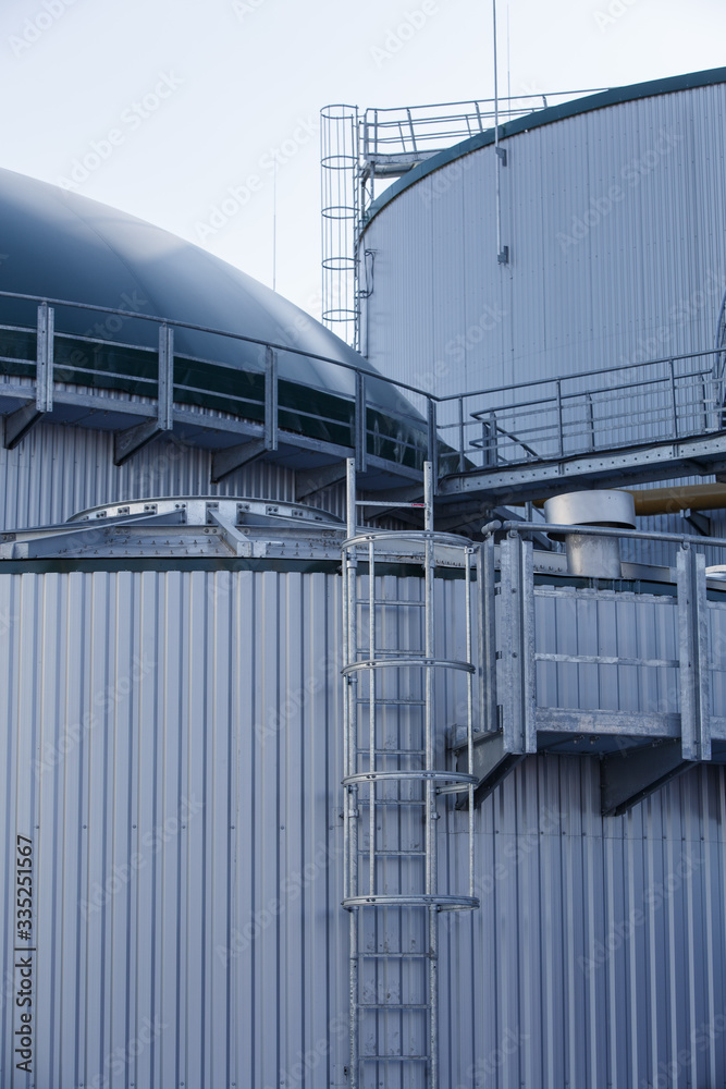 part of the metal industrial tanks outdoor. roof of technological building at the industrial plant on background. Equipment and appliances at the gas company. metal ladder stairs on the tank part of the metal industrial tanks outdoor. roof of technological building at the industrial plant on background. Equipment and appliances at the gas company. metal ladder stairs on the tank