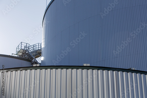 part of the metal industrial tanks outdoor. roof of technological building at the industrial plant on background. Equipment and appliances at the gas company. metal ladder stairs on the tank