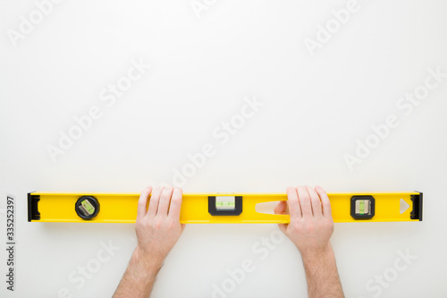 Man hands holding yellow spirit level on light gray table background. Building tool for floor, wall, ceiling or other surfaces level precision. Point of view shot. Empty place for text. Top down view. photo