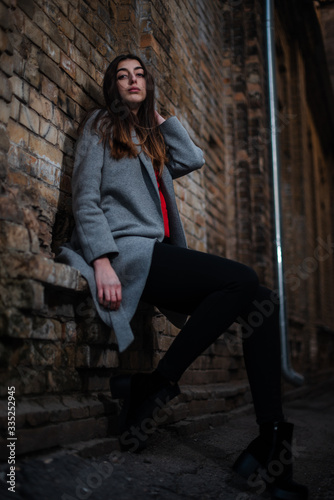 Girl in a red blouse and a gray cardigan on the background of the old brick wall © prokop.photo