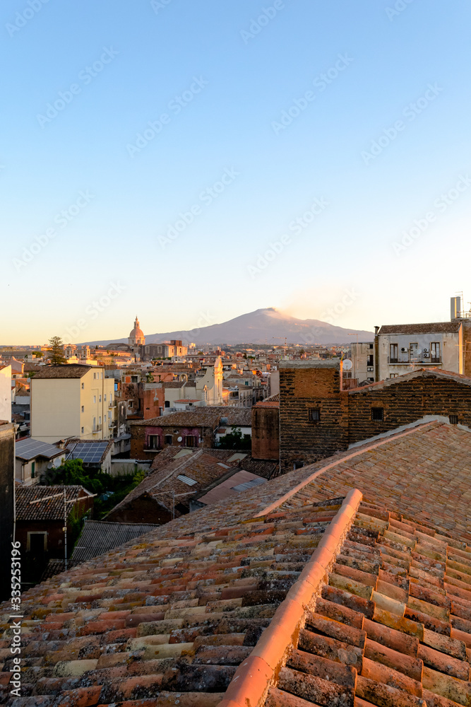 Catania, Sicily in Italy. Aerial view of the city roofs at sunset with the incredible Etna vulcano smoking in the background, nice warm colors and soft light.