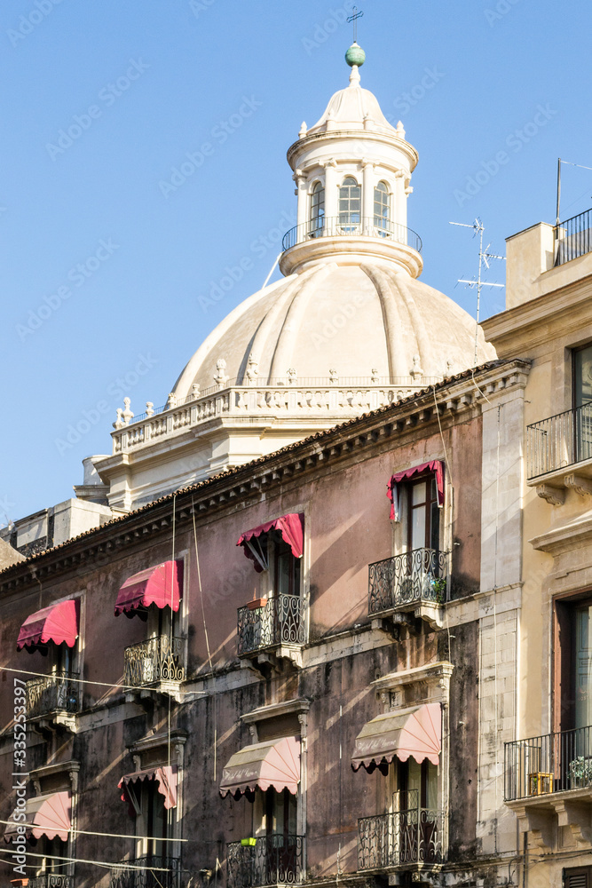 Catania, Sicily in Italy. City detail of one building in the main square with nice red window shades and a huge dome of a church in the background