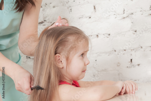 mother combing her comb little three-year-old girl