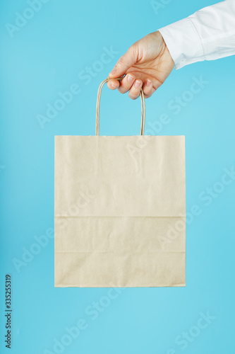 Paper bag at arm's length, brown craft bag for takeaway isolated on blue background. Packaging template layout with space for copying, advertising.