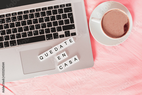 inscription stay home in spanish - quedate en casa, laptop and cup with coffee on the bed  photo