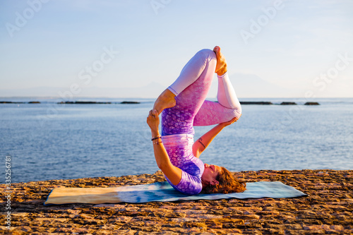 Young woman practicing Niralamba Sarvangasana, Shoulderstand. Inverted asana in hatha yoga. Yoga retreat. Bali, Indonesia photo