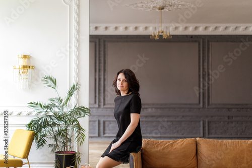 Woman in a black dress sits on the back of a sofa in the interior