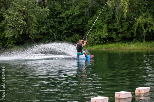 Man wakeboarding on river on summer day in jacket. Soft focus. Action blur.