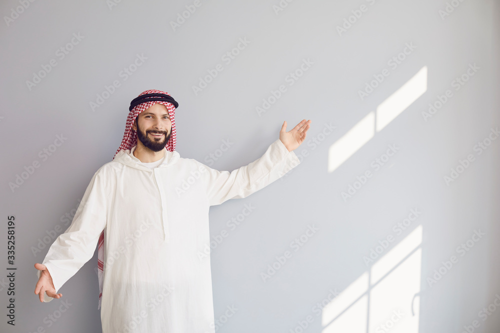 Attractive smiling arab man points his hand to a gray background