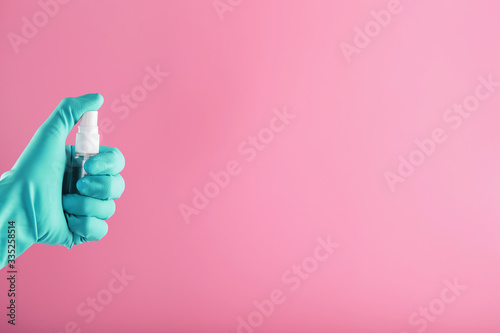 A blue-gloved hand holds a disinfectant on a pink background. Antiseptic treatment of hands from bacteria Sanitizer.