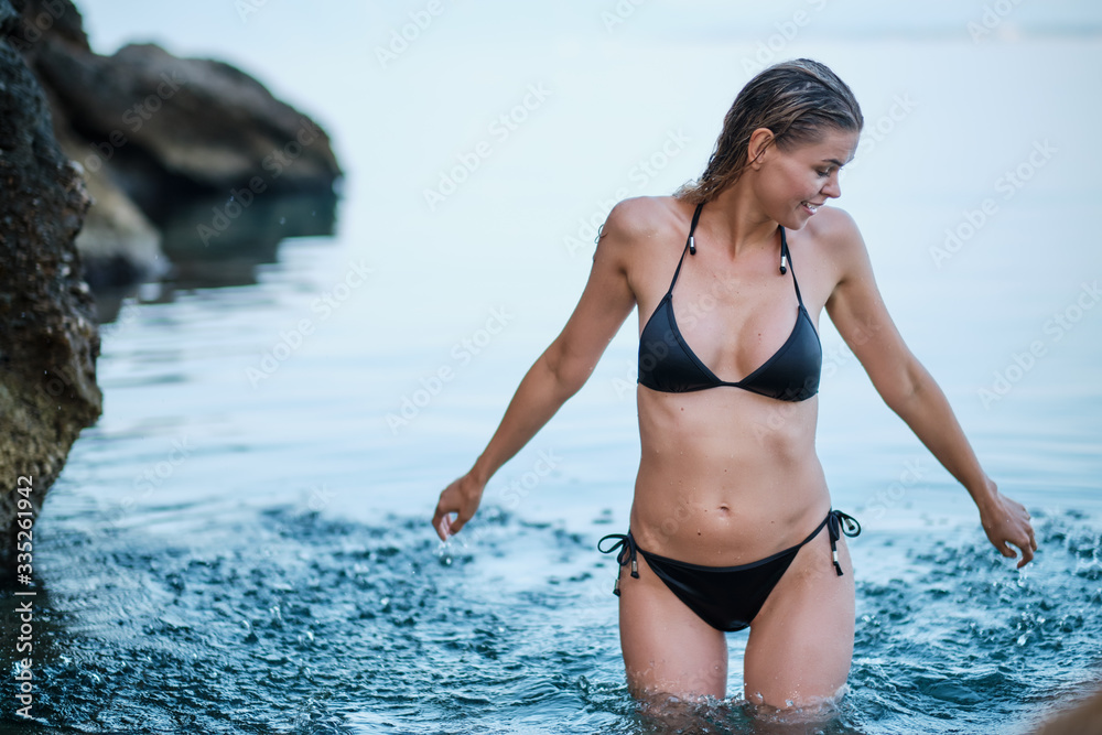 Summer lifestyle portrait of pretty young woman having fun on a tropical beach, splashing sea water. Wearing stylish swimsuit. Enjoying life and sunbathing Summer lifestyle portrait of pretty young woman having fun on a tropical beach, splashing sea water. Wearing stylish swimsuit. Enjoying life and sunbathing