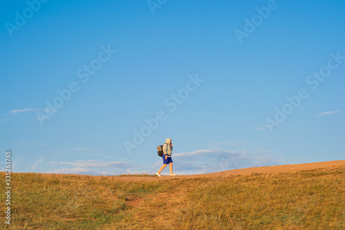 A backpacker with a backpack walks along the top of a hill amid a blue sky and clouds. Summer evening. Sunset.