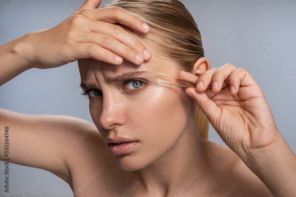 Attentive young female person pinching her eyebrows