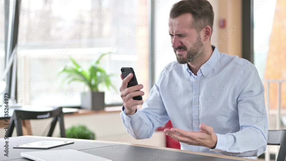 Young Man Reacting to Loss on Smartphone in Office Young Man Reacting to Loss on Smartphone in Office