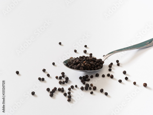 black peppercorns on metal spoon in white background 