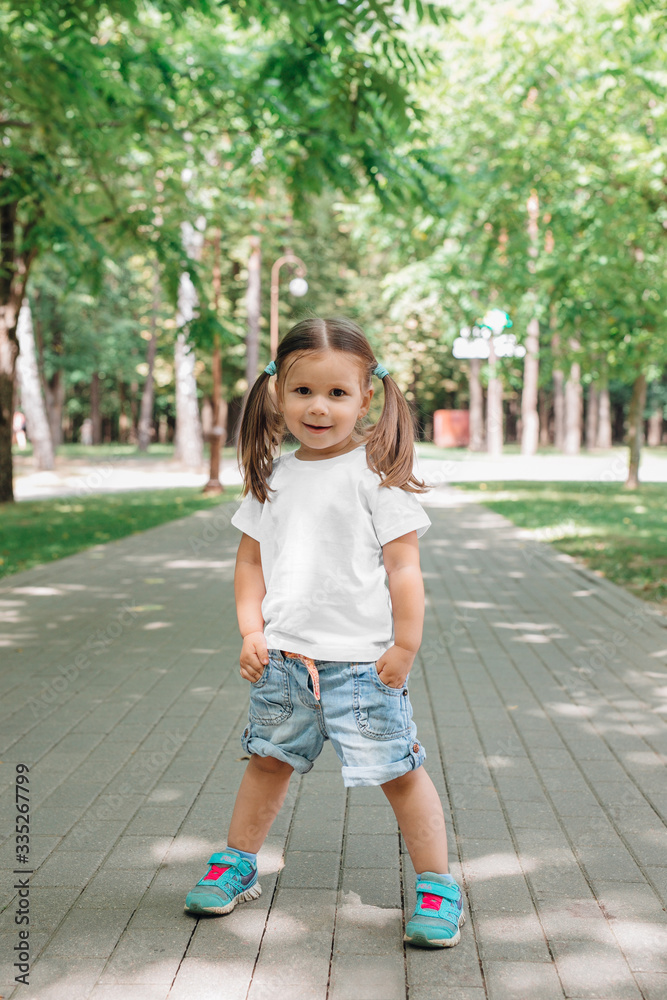 Beautiful little girl dressed in t-white shirt and jeans stand in park