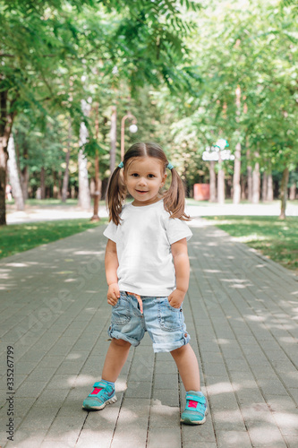 Beautiful little girl dressed in t-white shirt and jeans stand in park © Elena Kratovich