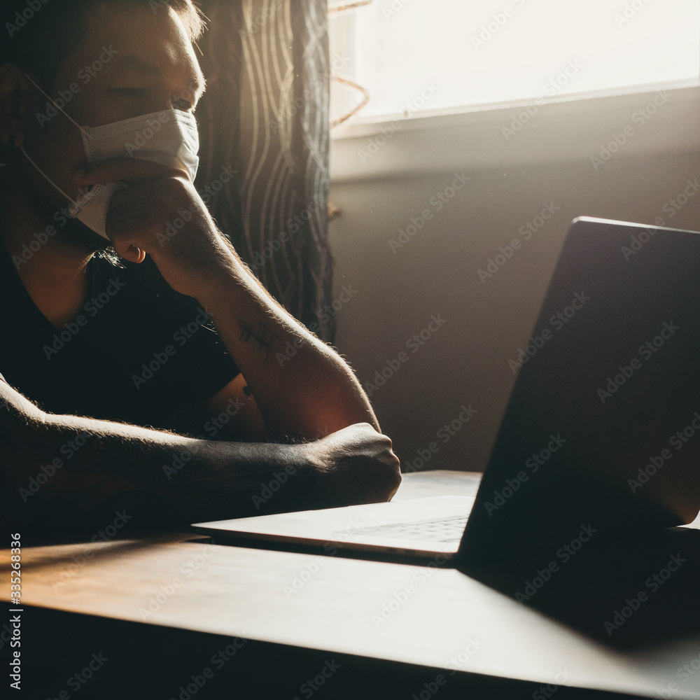 Obraz premium A asian man in medical mask working on laptop in dark area. Thinking gesture.