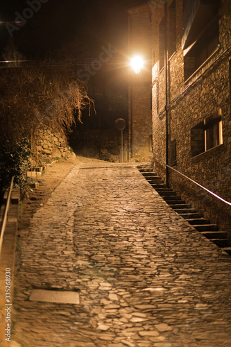 Night empty streets of Andorra La Vella paved with ancient masonry are lit by a bright lantern in February.