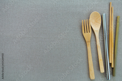 Reusable and environmentally friendly utensils, including bamboo spoon, fork, chopsticks, straw and stainless straw on the side of beige or gray background. Copy space.