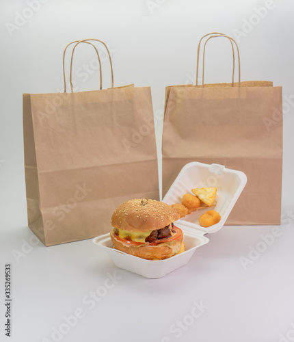 hamburger in a takeaway container and a paper bag on a white background.