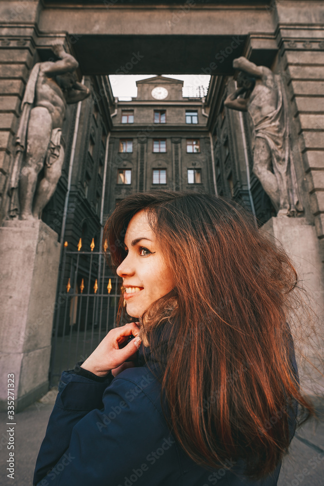 Obraz premium Portrait of a girl with long hair in a jacket against the background of an old historical building in St. Petersburg, an architectural monument with sculptures and columns