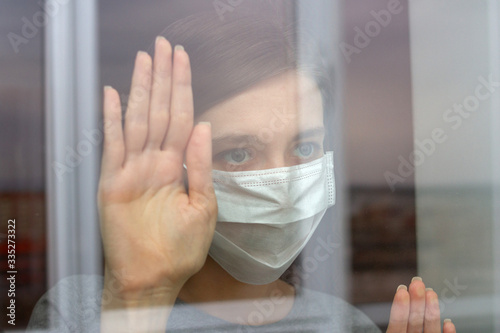 young woman in medical mask looking through window